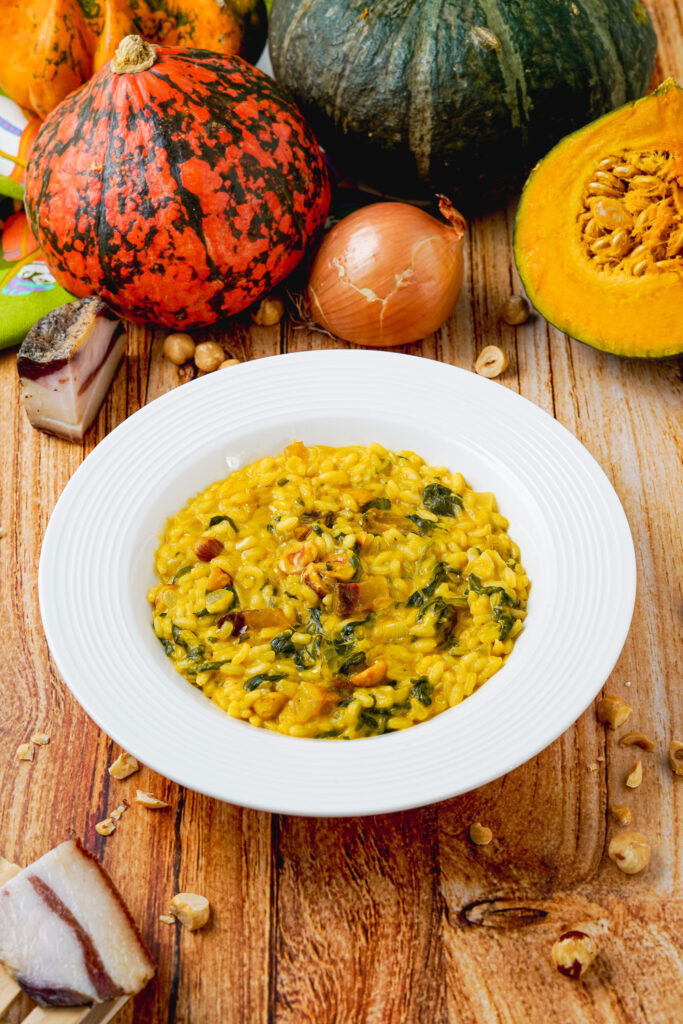 risotto nel piatto bianco sul tavolo in legno con pezzo di guanciale zucca e nocciole