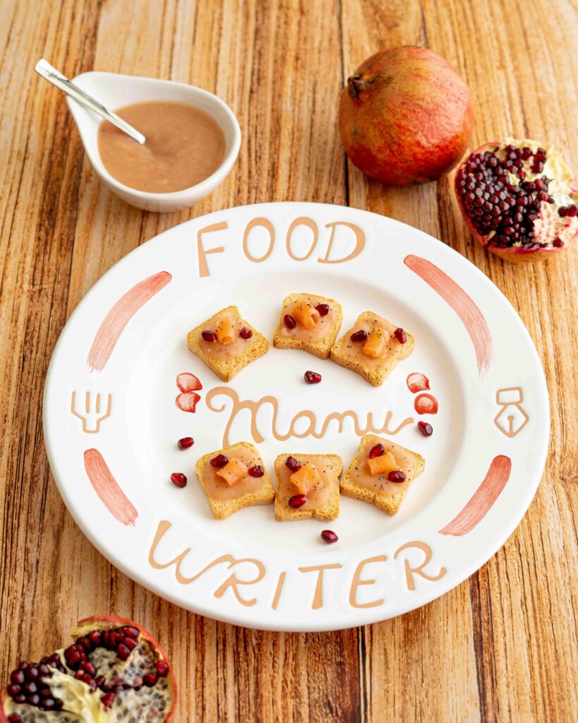 Piatto in ceramica con mini toast di crema al ravanello e salmone sul tavolo con melagrana aperta