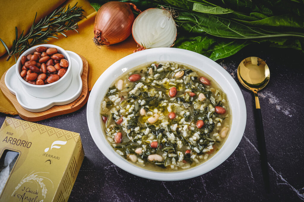 piatto con la minestra, ciottola con fagioli, cucchiaio e cipolla e bietola cruda.