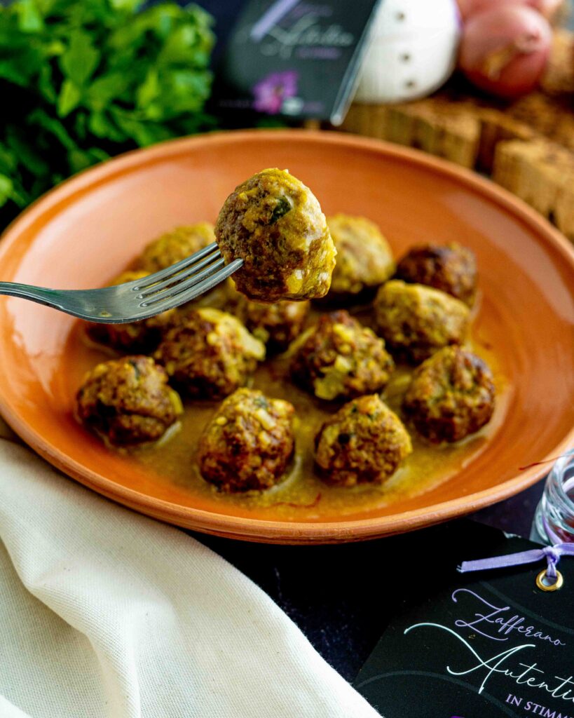 polpette allo zafferano dentro piatto cn mestolo e zafferano e cipolla con strofinaccio