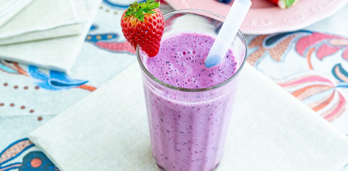 frullato nel bicchiere su un tovagliolo e tovaglia colorata un piatt oin lontananza con fragole e mirtilli