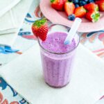 frullato nel bicchiere su un tovagliolo e tovaglia colorata un piatt oin lontananza con fragole e mirtilli