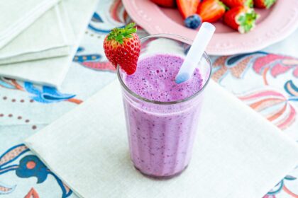 frullato nel bicchiere su un tovagliolo e tovaglia colorata un piatt oin lontananza con fragole e mirtilli
