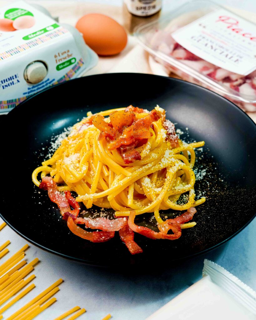 scatola di uova e scatola di guanciale con piatto nero e spaghetti e uovo e contenitore nero
