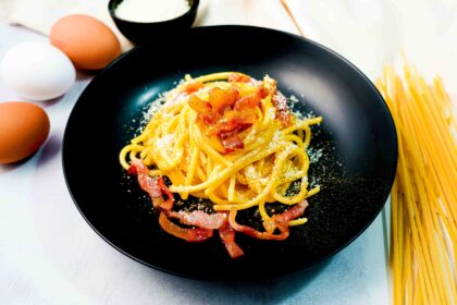 piatto di pasta alla carbonara nero, sul tavolo bianco con uova e spaghettoni e formaggio