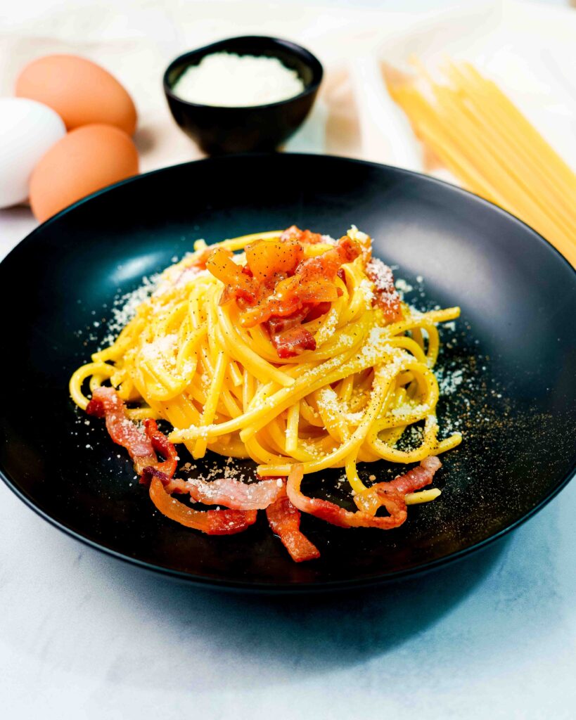 primo piano del piatto con pasta e uova e spaghetti sul tavolo con contenitore di formaggio