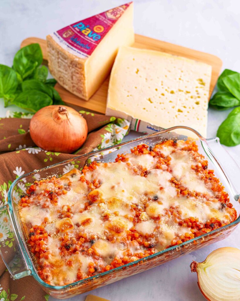 teglia con fregola con sul tavolo pezzi di formaggi sul tagliere e cipolle e basilico ricetta sarda succu instuvadu