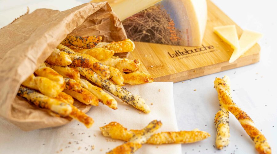 grissini dentro una busta di carta aperta con formaggio nel tagliere e sul tavolo qualche grissino