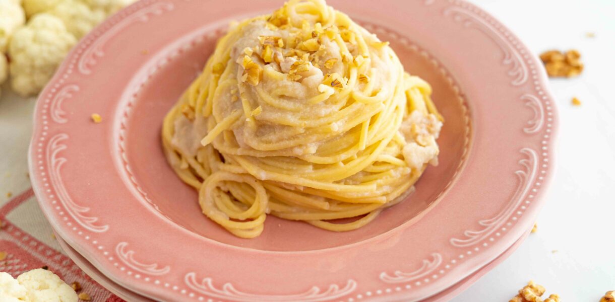 spaghetti sul piatto fondo rosa, nel tavolo cavolfiore aperto e noci