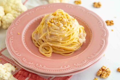 spaghetti sul piatto fondo rosa, nel tavolo cavolfiore aperto e noci