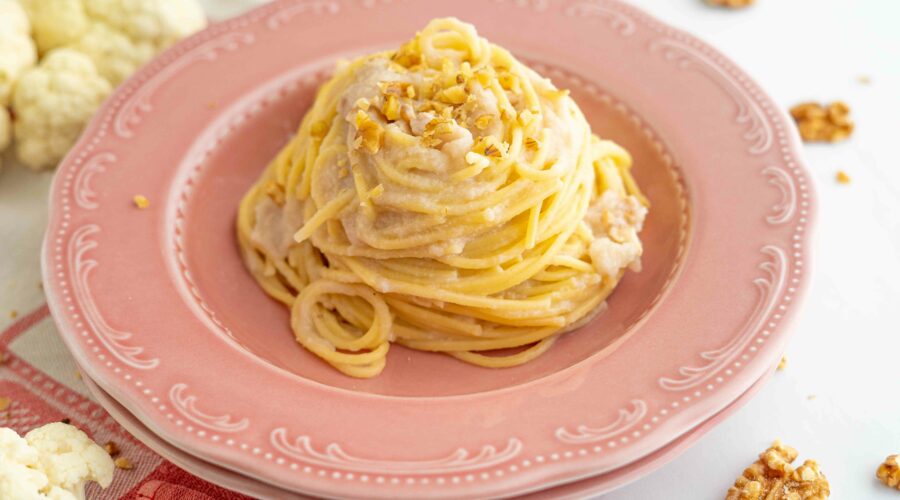 spaghetti sul piatto fondo rosa, nel tavolo cavolfiore aperto e noci