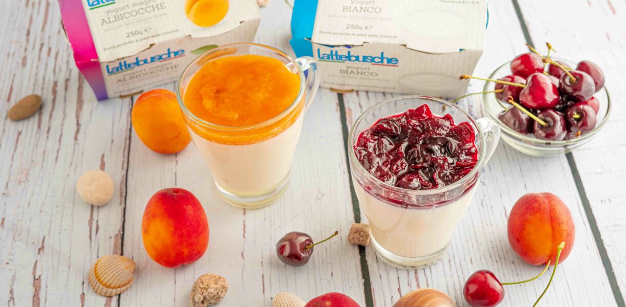 bicchiere con budino due confezioni di yogurt sul tavolo albicocche e ciliegie in ciotola