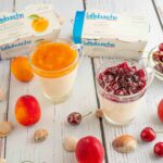 bicchiere con budino due confezioni di yogurt sul tavolo albicocche e ciliegie in ciotola