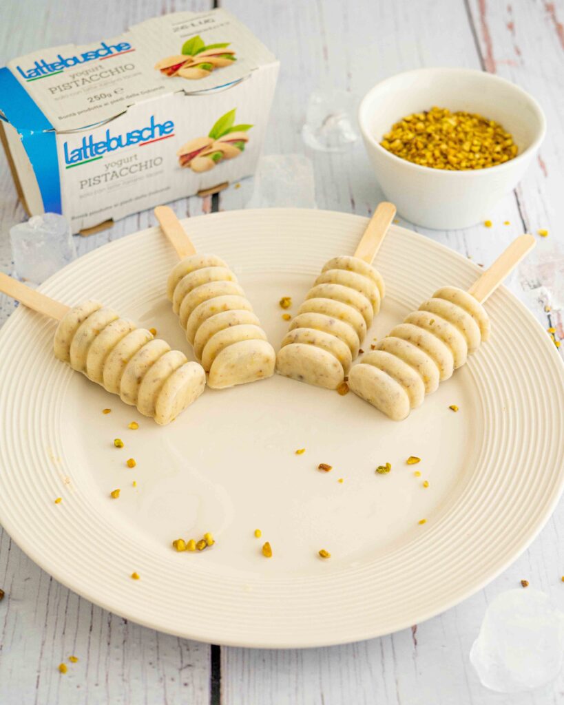 ghiaccioli al pistacchio affusolati sul piatto, sul tavolo ciottola di pistacchi e confezione di yogurt con cubetti di ghiaccio