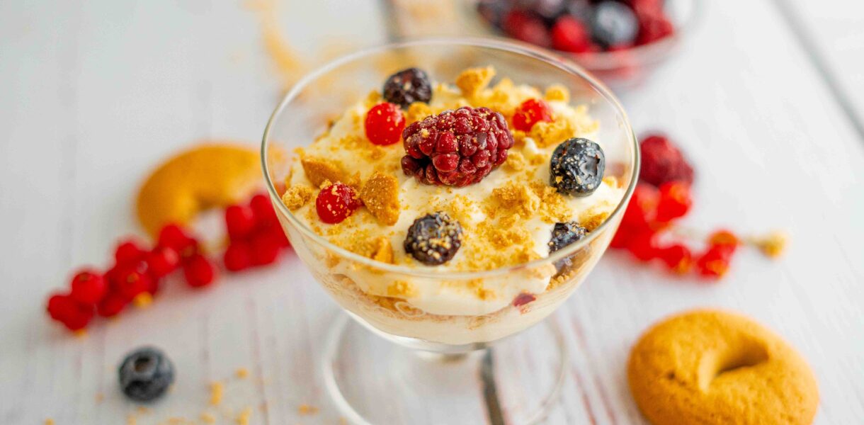 coppa con biscotti e mascarpone e frutti di bosco, sul tavolo frutti di bosco e biscotti