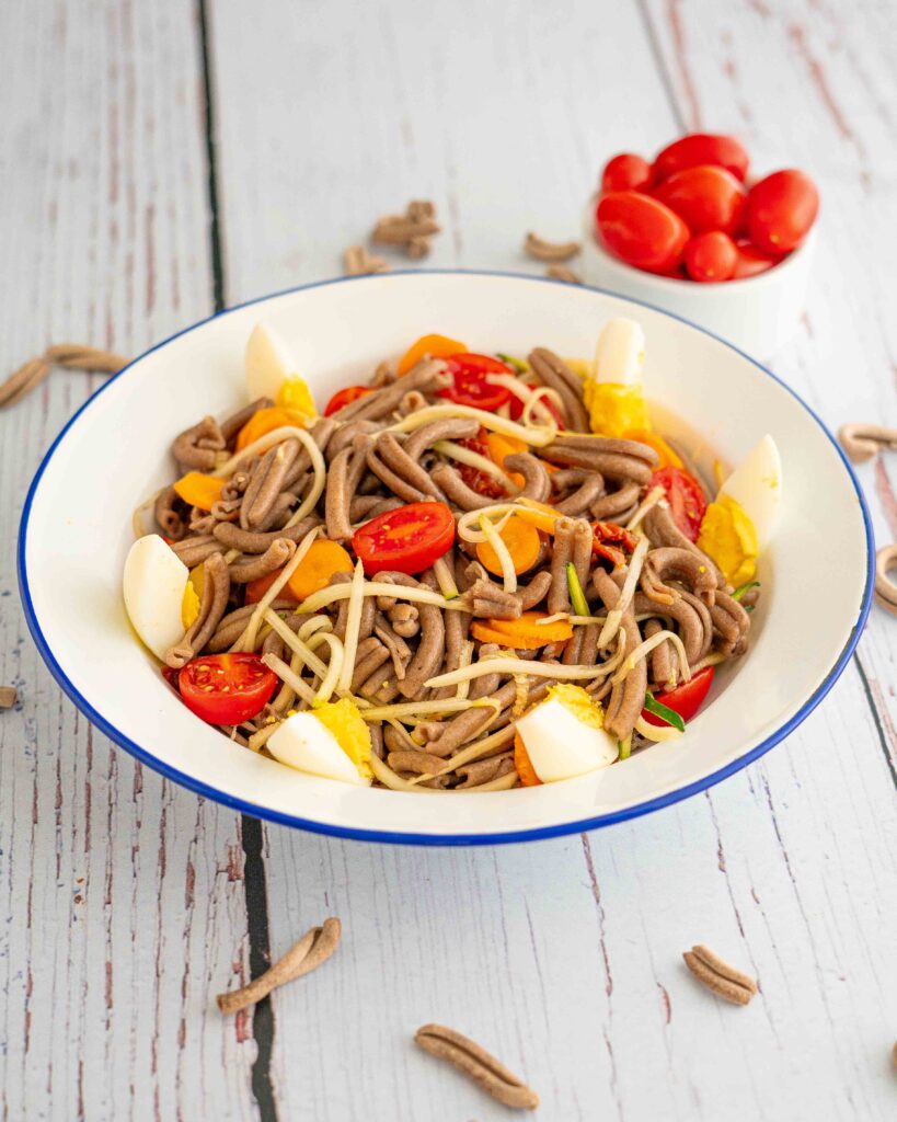 piatto con pasta uovo pomodori e zucchine sul tavolo pasta cruda e ciotola di pomodorini datterino
