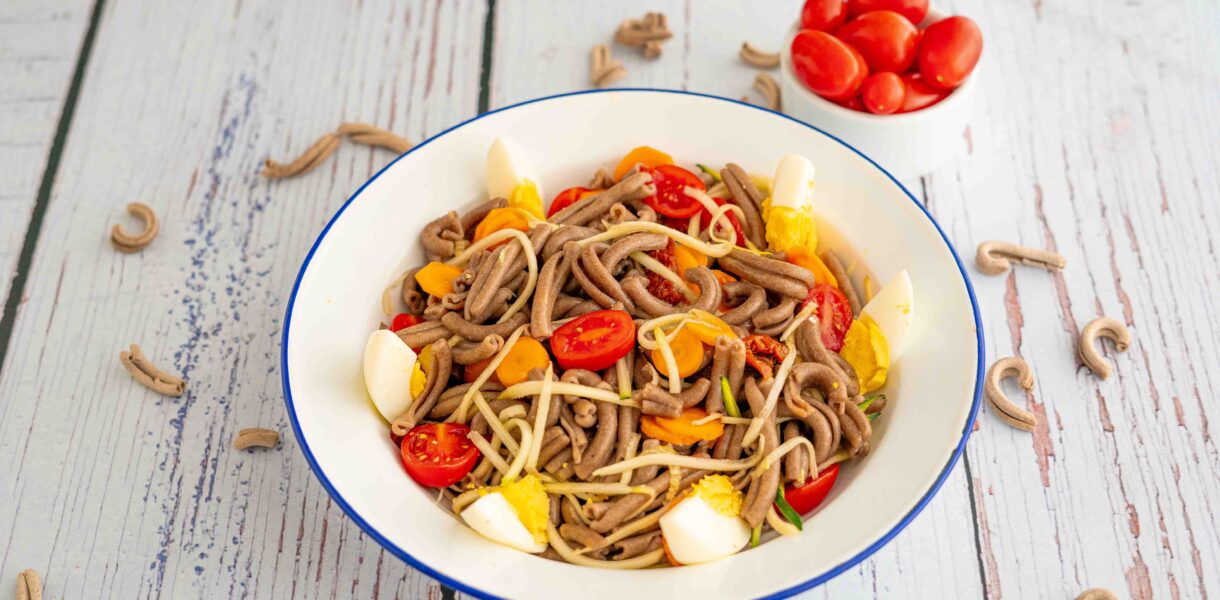piatto con pasta uovo pomodori e zucchine sul tavolo pasta cruda e ciotola di pomodorini datterino