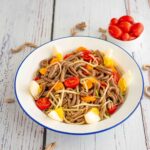 piatto con pasta uovo pomodori e zucchine sul tavolo pasta cruda e ciotola di pomodorini datterino