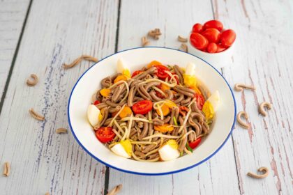 piatto con pasta uovo pomodori e zucchine sul tavolo pasta cruda e ciotola di pomodorini datterino