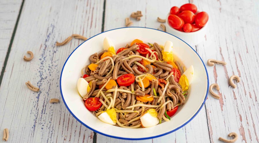 piatto con pasta uovo pomodori e zucchine sul tavolo pasta cruda e ciotola di pomodorini datterino