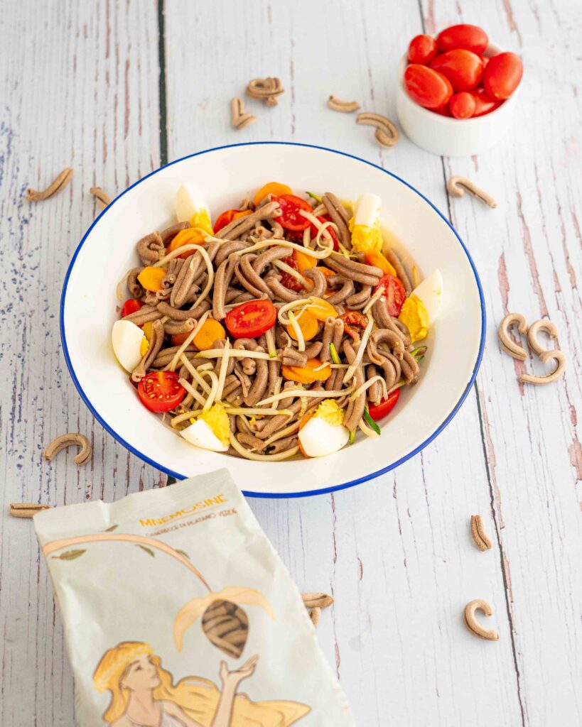 foto piatto con pasta uovo pomodori e zucchine sul tavolo pasta cruda e ciotola di pomodorini datterino e pacco di pasta
