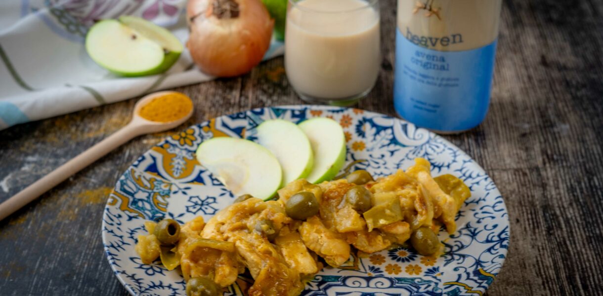 pollo nel piatto sl tavolo con cucchiaio di curry mela cipolla un bicchiere di latte e bottiglia di latte