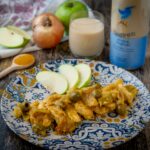 pollo nel piatto sl tavolo con cucchiaio di curry mela cipolla un bicchiere di latte e bottiglia di latte