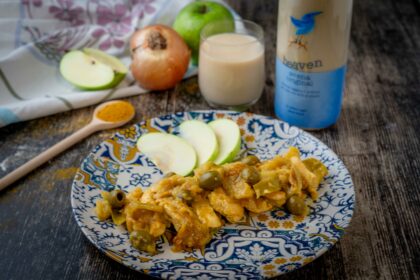 pollo nel piatto sl tavolo con cucchiaio di curry mela cipolla un bicchiere di latte e bottiglia di latte