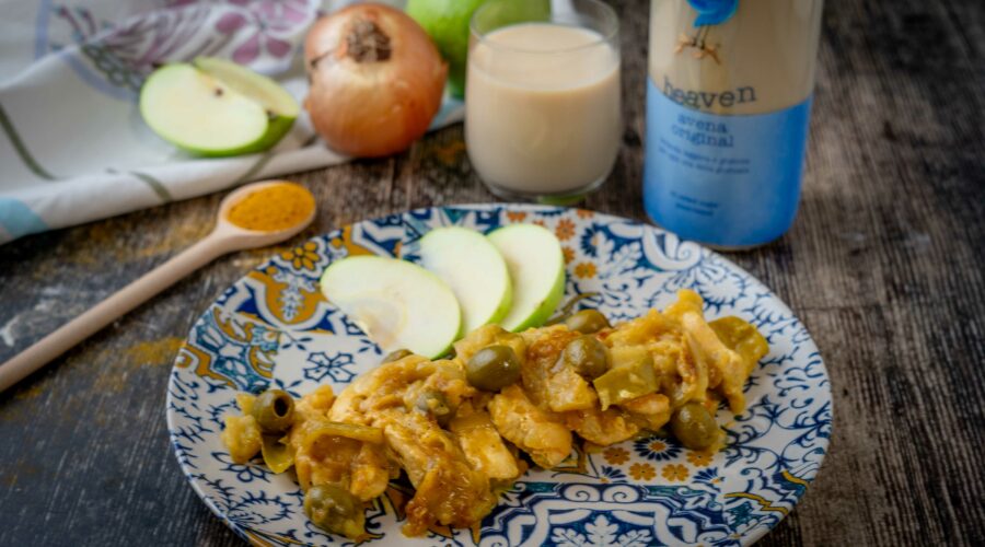 pollo nel piatto sl tavolo con cucchiaio di curry mela cipolla un bicchiere di latte e bottiglia di latte