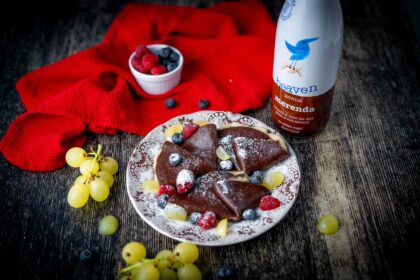 crepe sul piatto piccolo al cioccolato sul tavolo botiia di latte al cioccolato uva strofinaccio e frutti rossi