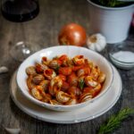 nel piatto bianco lumache al sugo sul tavolo calice divino rosso una cipolla aglio e strofinaccio