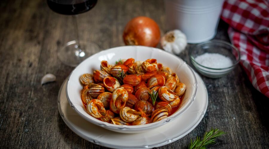 nel piatto bianco lumache al sugo sul tavolo calice divino rosso una cipolla aglio e strofinaccio