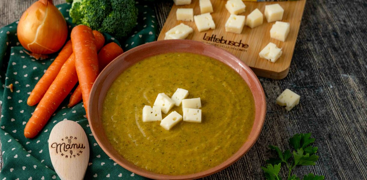 VELLUTATA DIVERDE SUL PIATTO CAROTE SU TAVOLO CON BROCCOLO CRUDO E CIPOLLA TAGLIERE CON FORMAGGIO