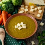 VELLUTATA DIVERDE SUL PIATTO CAROTE SU TAVOLO CON BROCCOLO CRUDO E CIPOLLA TAGLIERE CON FORMAGGIO