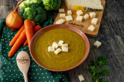 VELLUTATA DIVERDE SUL PIATTO CAROTE SU TAVOLO CON BROCCOLO CRUDO E CIPOLLA TAGLIERE CON FORMAGGIO