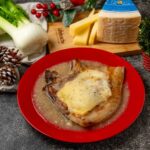 brciola di maiale con formaggio sciolto nel piatto rosso sul tavolo addobbi natalizi e pezzo di formaggio