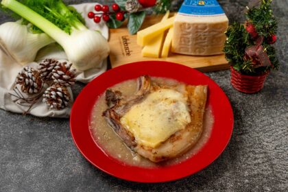 brciola di maiale con formaggio sciolto nel piatto rosso sul tavolo addobbi natalizi e pezzo di formaggio