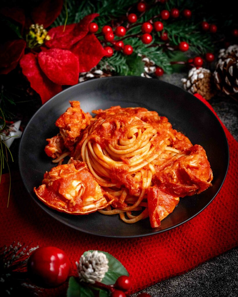piatto nero dentro linguine al sugo rosso di aragosta, sul tavolo addobbi di natale e strofinaccio rosso.