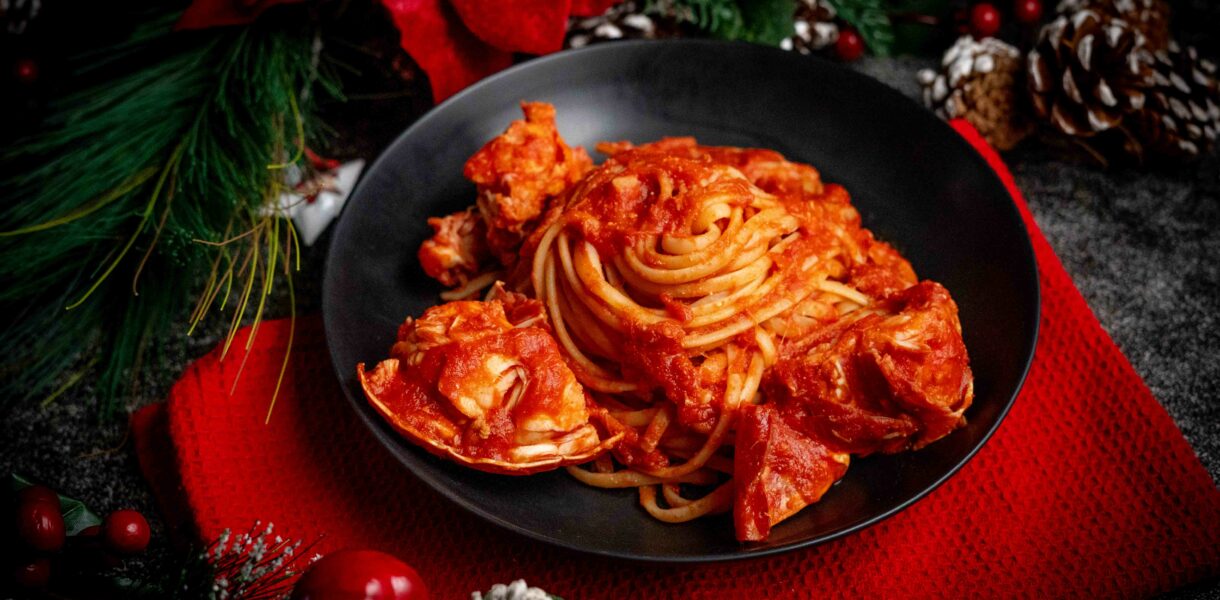 linguine al sugo di aragosta nel piatto nero sul tavolo strofinaccio rosso con addobbi di natale