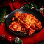 linguine al sugo di aragosta nel piatto nero sul tavolo strofinaccio rosso con addobbi di natale