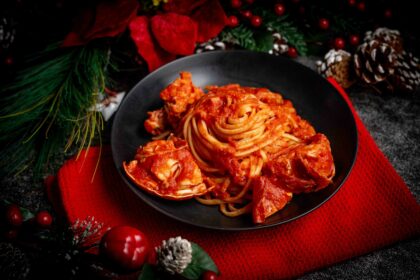 linguine al sugo di aragosta nel piatto nero sul tavolo strofinaccio rosso con addobbi di natale