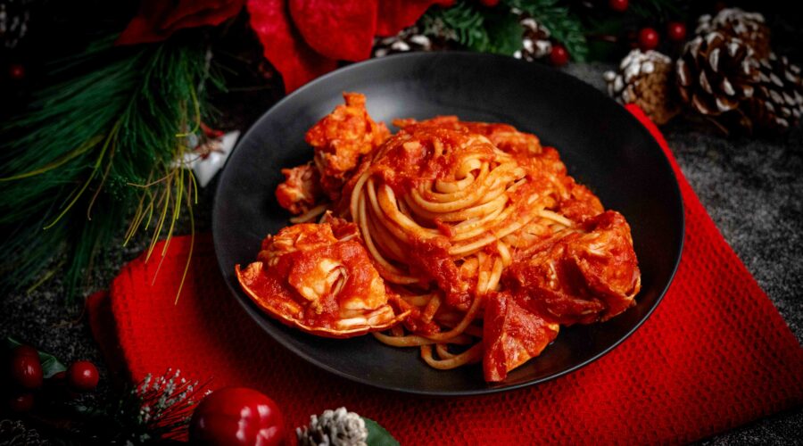 linguine al sugo di aragosta nel piatto nero sul tavolo strofinaccio rosso con addobbi di natale