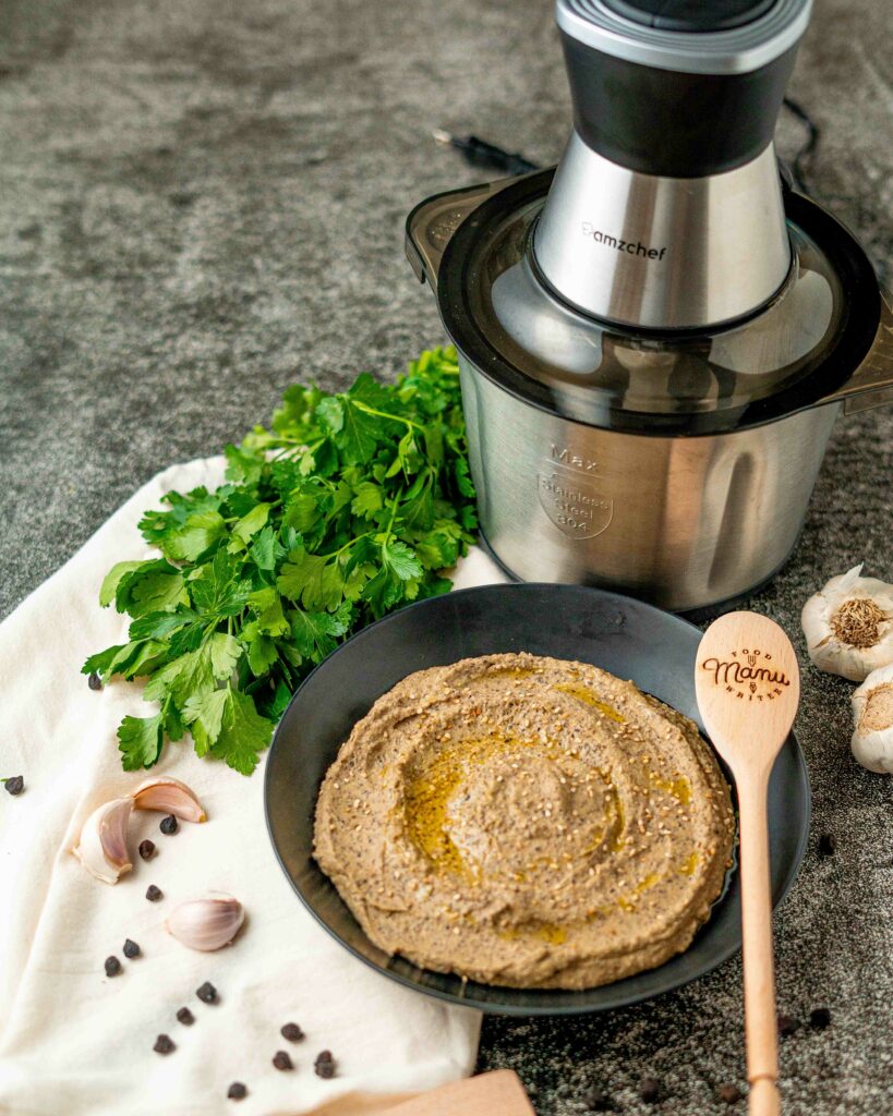 piatto nero con hummus nel piatto con ceci sullo strofinaccio e nel tavolo tritattuto in acciaio grande