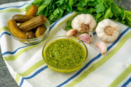 ciotola con salsa verde con ciotola di cetrioli sul tavolo stroniaccio e teste di aglio e prezzemolo
