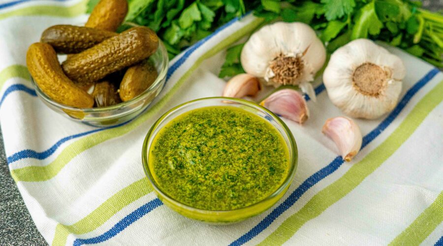 ciotola con salsa verde con ciotola di cetrioli sul tavolo stroniaccio e teste di aglio e prezzemolo
