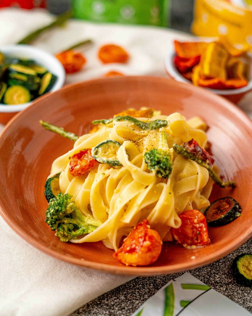 Tagliatelle con chips di verdure nel piatto di terracotta in primo piano