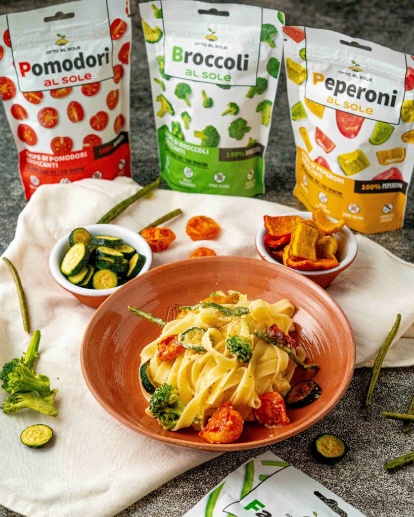 Tagliatelle con chips di verdure piatto di pasta nel piatto in terracotta con lew buste delle verdure disidratate in confezione chiusa peperoni broccoli e fagiolini