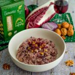 riso nel piatto con scatola di riso e bicchiere di vino rosso e noci e radicchio sul tavolo